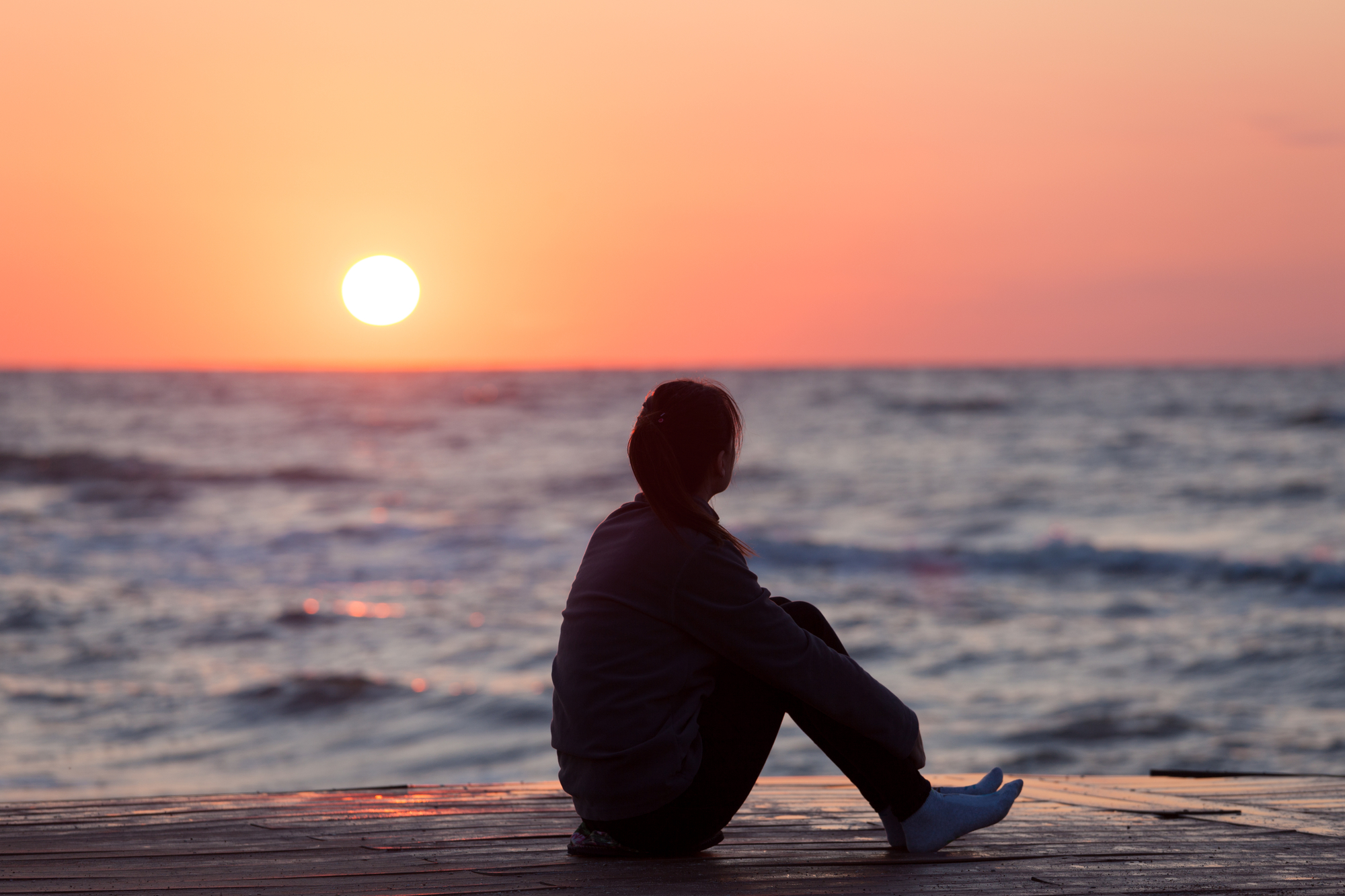 Woman sitting on the beach at sunset.