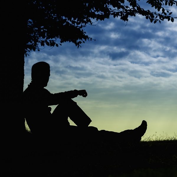 man sitting under a tree at sunset in pensive thought