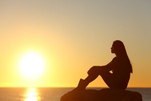 silhouette of a sad woman sitting looking at the sunset