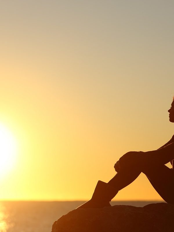 silhouette of a sad woman sitting looking at the sunset