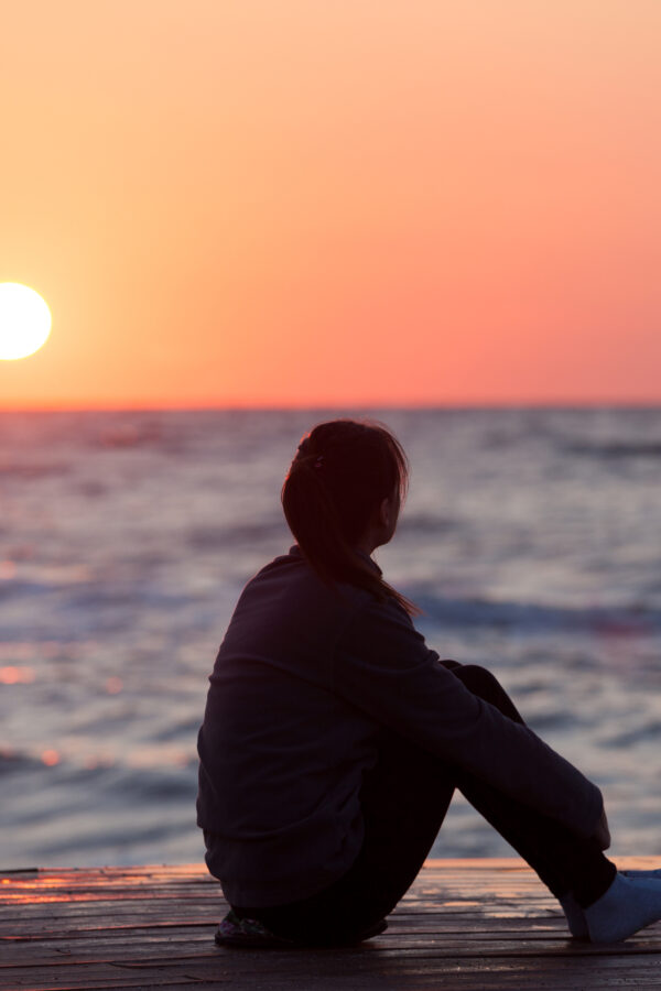 Woman sitting on the beach at sunset.